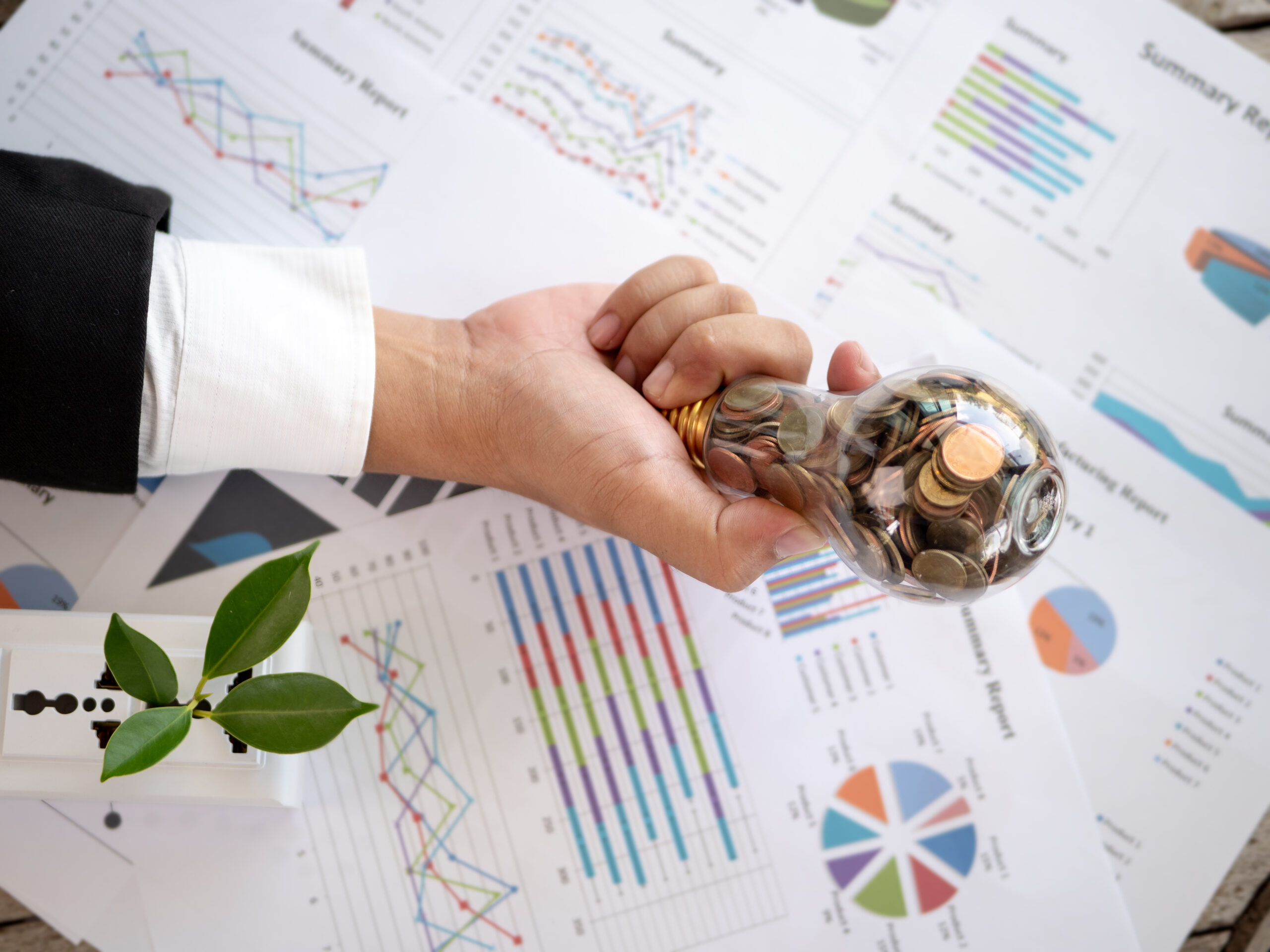 Hand holding a lightbulb filled with coins over financial charts, symbolizing patient capital, long-term investing, and strategic wealth growth