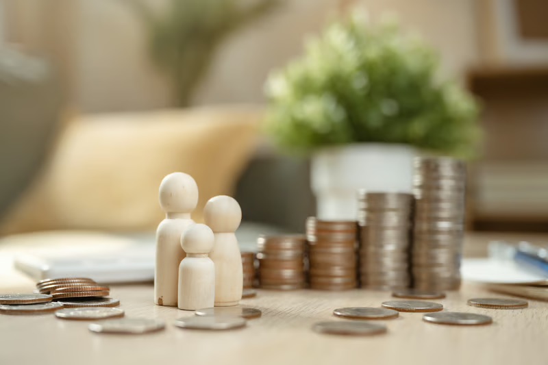 Wooden family figures beside growing stacks of coins representing generational wealth preservation and long-term financial planning.