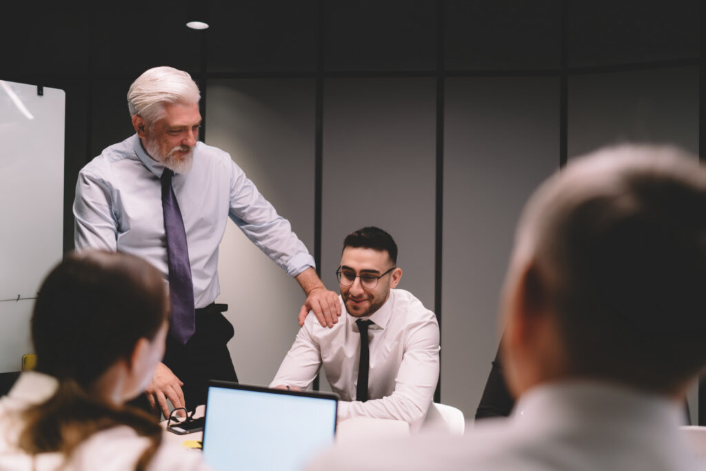 Senior business professional mentoring a younger colleague during a team meeting in a modern office.