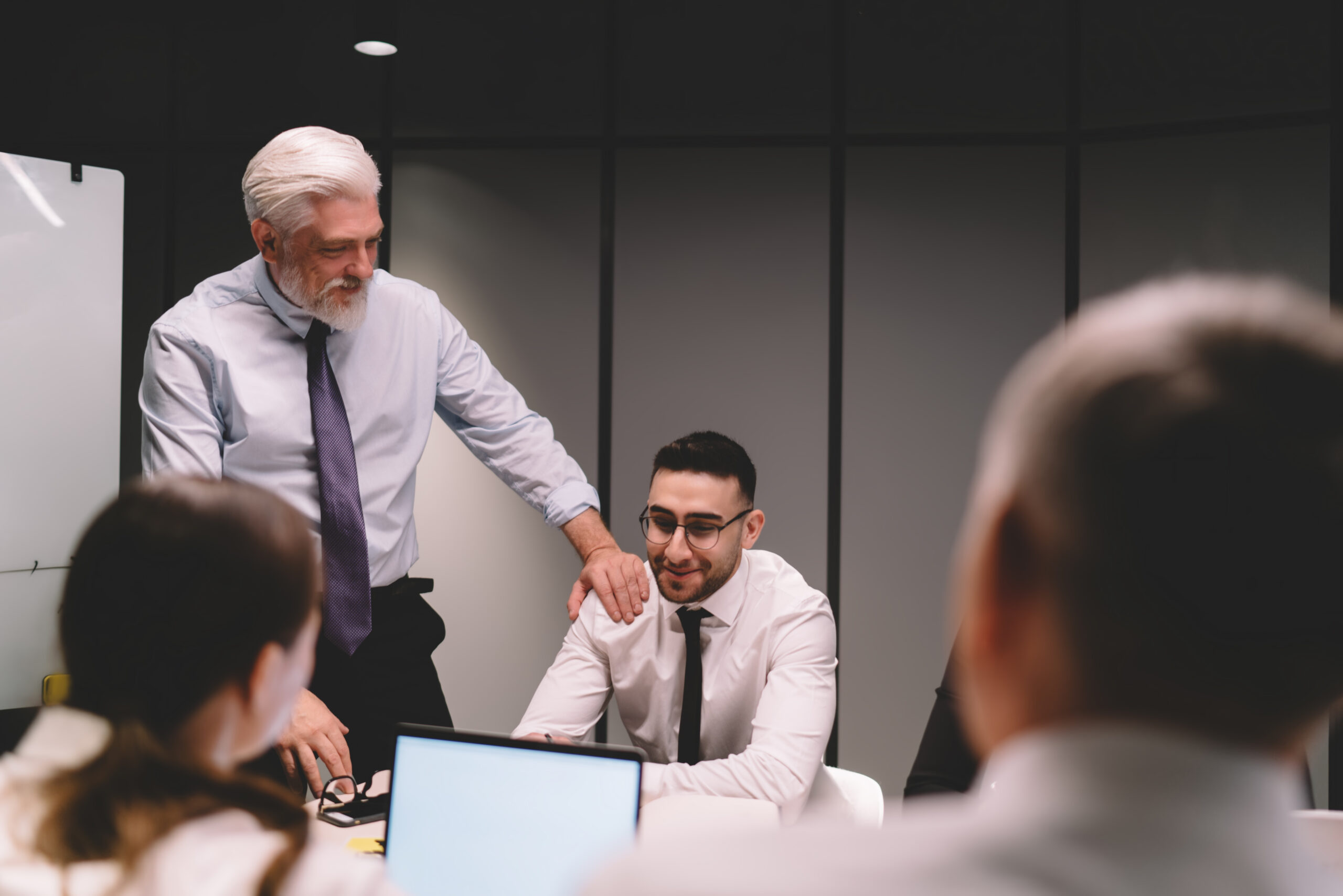 Senior business professional mentoring a younger colleague during a team meeting in a modern office.